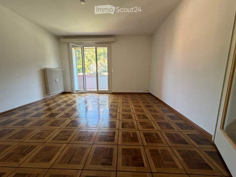 Empty room with wooden parquet flooring, white walls, and a large sliding glass door leading to a balcony.
