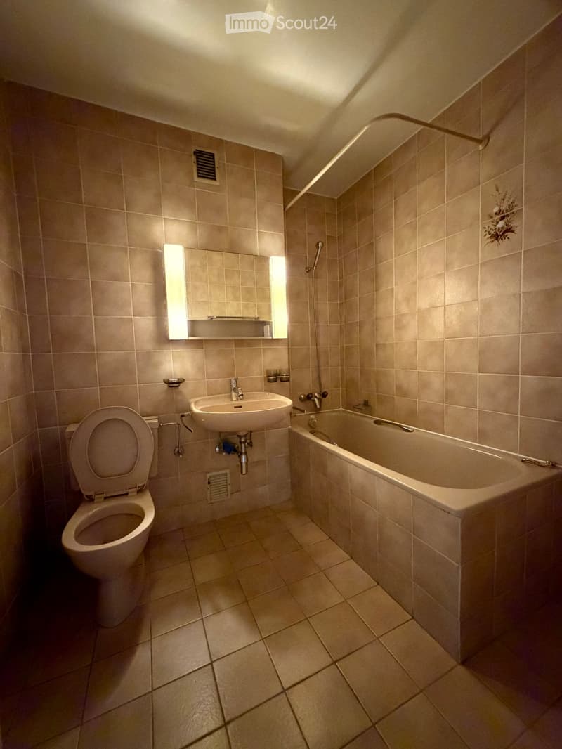 Bathroom with beige tiles, toilet, sink, bathtub, mirror, and light fixture.
