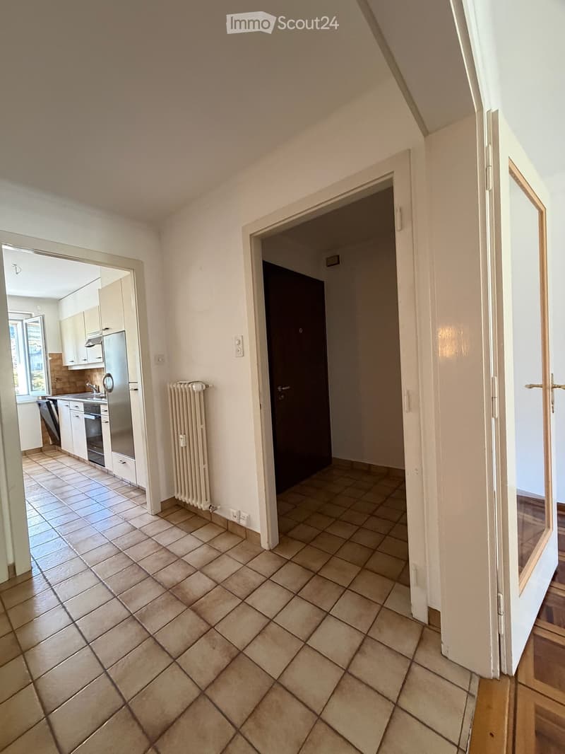 Empty hallway with tiled floor, white walls, and doors leading to a kitchen and another room.