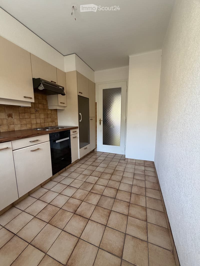 Empty kitchen with tiled floor, white cabinets, and a black oven. A door with a frosted glass panel is visible.