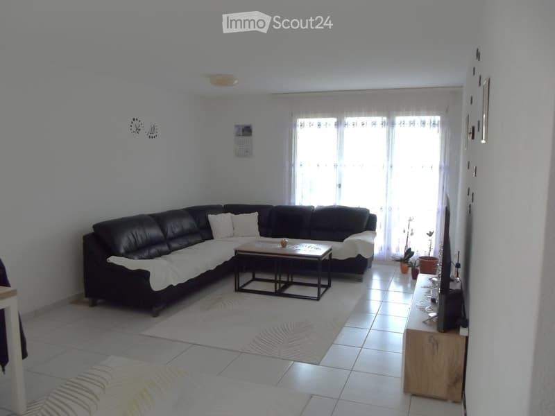 Modern living room with a black leather sectional sofa, a wooden coffee table, a TV stand, and a white rug.