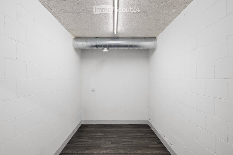 Completely empty room with white brick walls, dark wooden floor, and exposed metal ductwork on the ceiling.