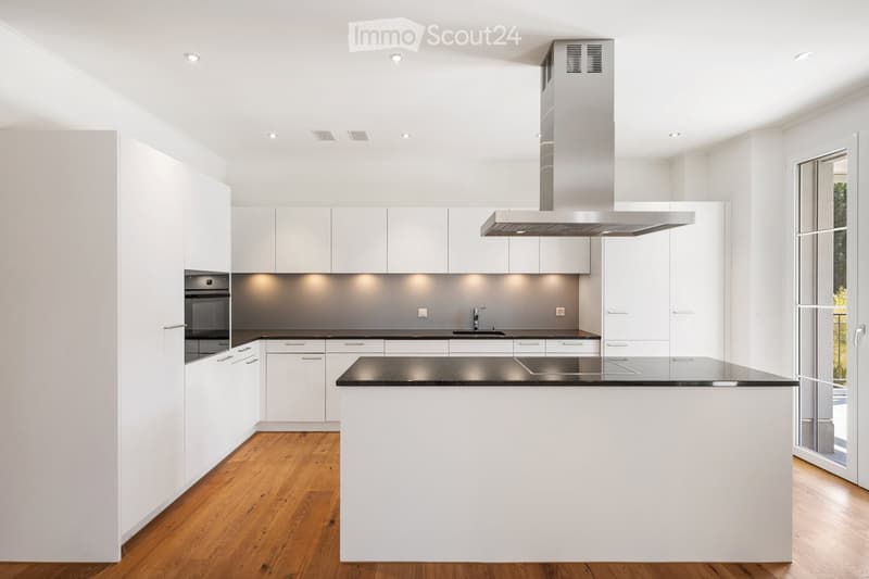 Modern kitchen with white cabinets, black countertops, and a central island. Features include an oven, sink, range hood, and ample storage space.
