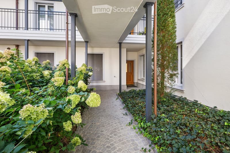 Courtyard view of a modern building with balconies, greenery, and a pathway leading to an entrance door.