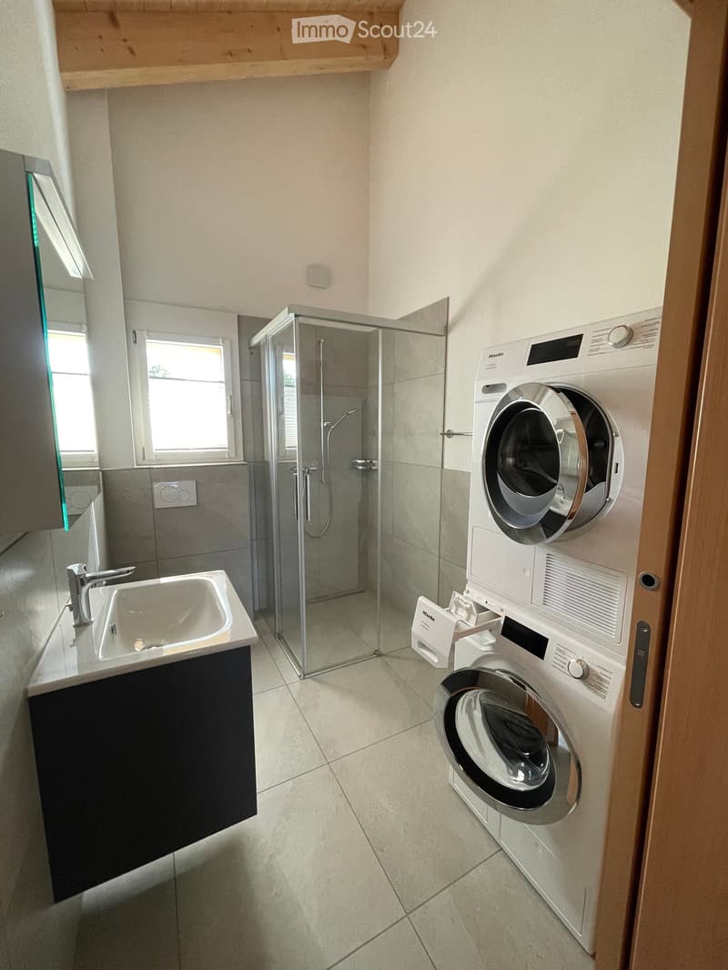 Modern bathroom with a sink, shower, and stacked washing/drying machine unit.