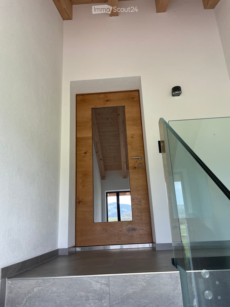 Modern hallway with wooden door, glass staircase railing, and sleek lighting fixture on the wall.