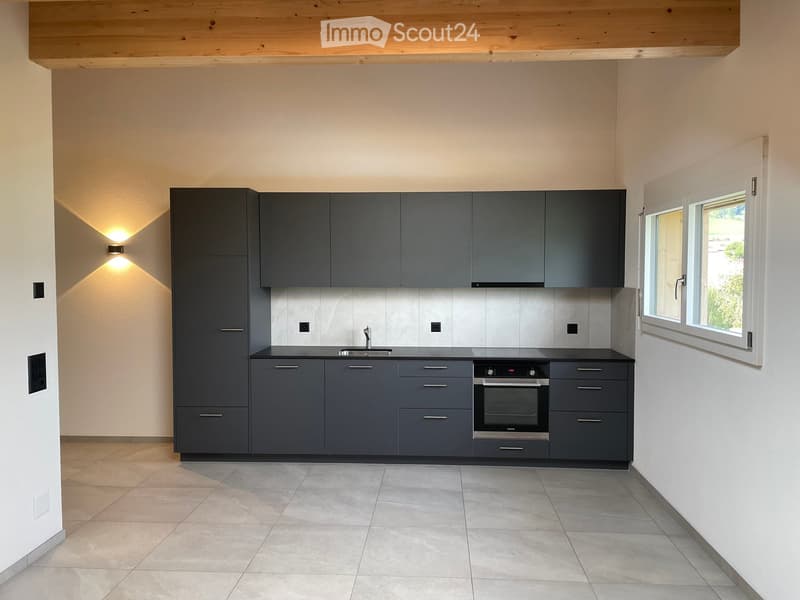 Modern kitchen with grey cabinets, stainless steel sink, oven, and tiled floor.