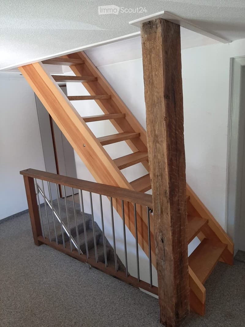 Wooden staircase with metal balustrade, light-colored wooden steps, and a central wooden post.