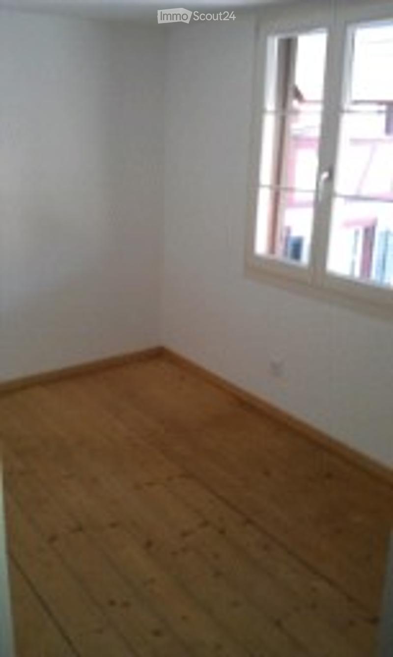 Completely empty room with wooden flooring and white walls. A single window with white frame is visible on one wall.
