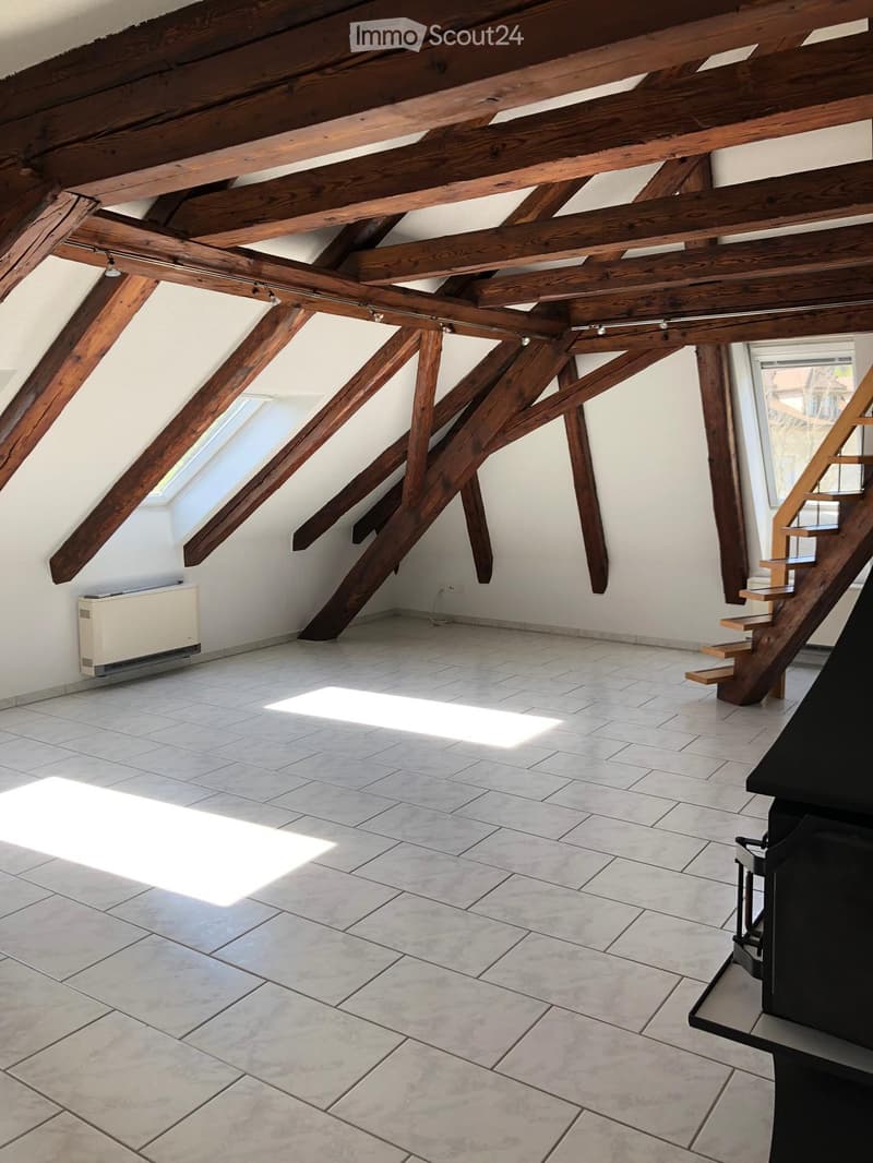 An attic space with exposed wooden beams, tiled floor, skylight windows, and a staircase leading upwards.