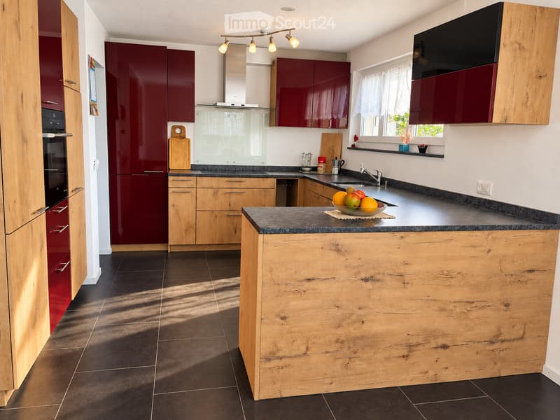 Modern kitchen with wooden and red cabinets, granite countertop, island, sink, refrigerator, and various kitchen items.