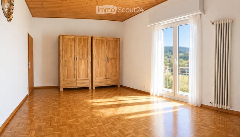 Empty room with wooden flooring, white walls, large windows with white curtains, and two wooden wardrobes.