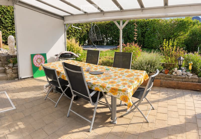A covered outdoor patio with a dining table and chairs, surrounded by lush greenery and garden decorations.