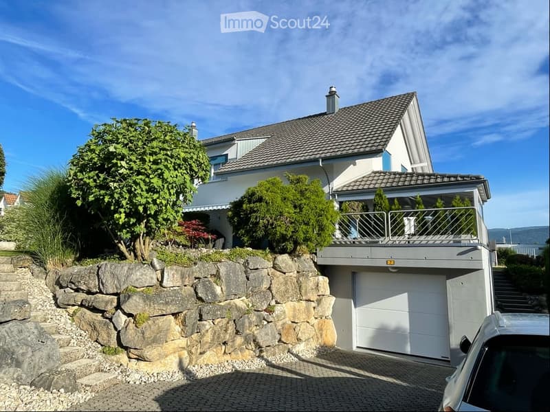 Two-story house with a garage, raised ground floor, and a balcony overlooking the garden.