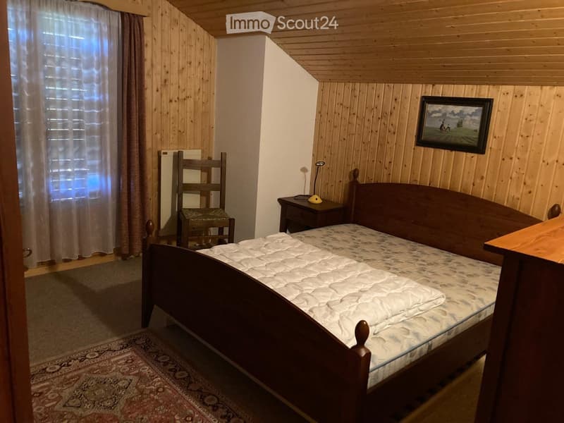 Cozy wooden bedroom with a single bed, nightstand, chair, and a picture frame on the wall.