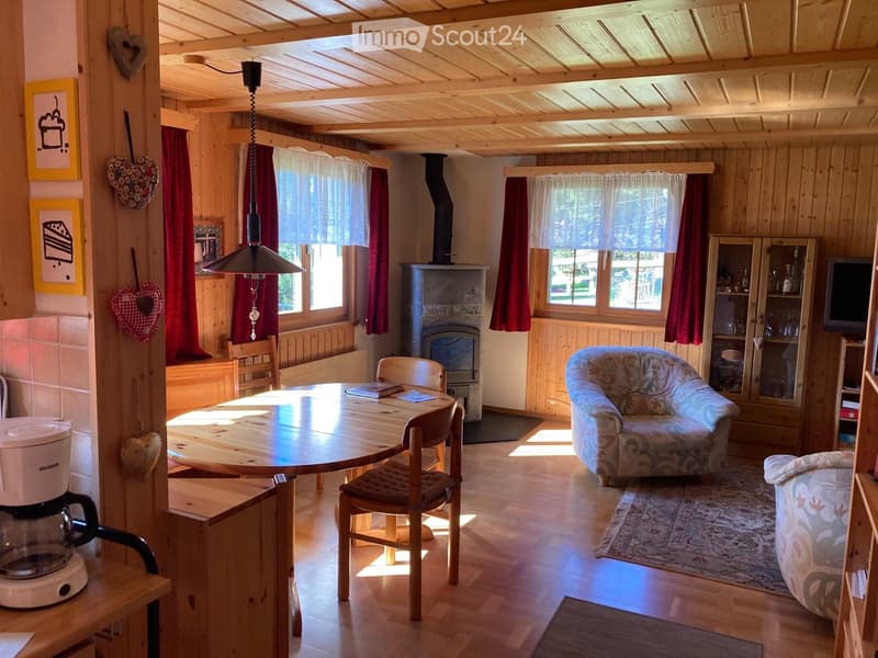 Cozy living room with wooden beams, fireplace, sofa, armchair, dining table, and coffee maker.