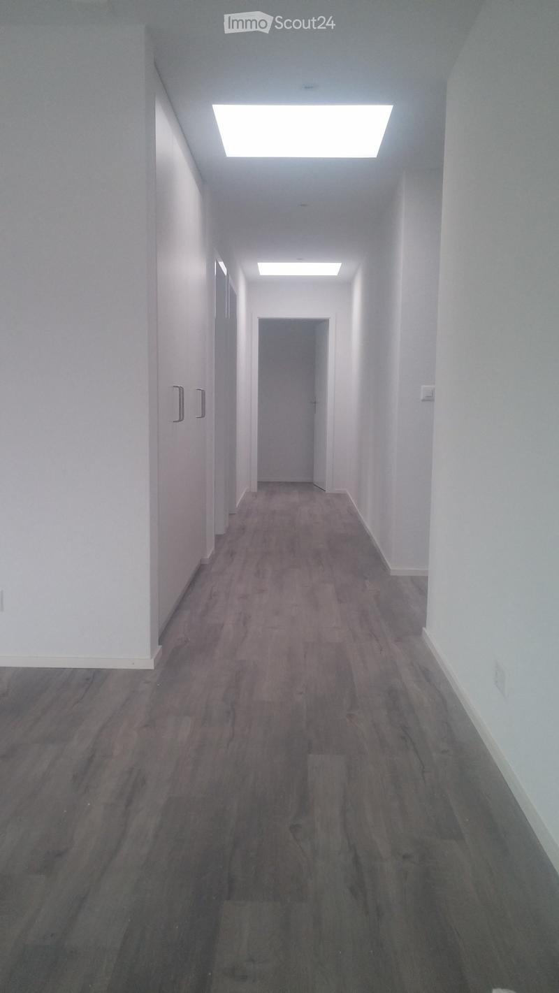 Empty hallway with wooden flooring, white walls, and recessed lighting. Features a closed door at the end and a partially open door on the left side.
