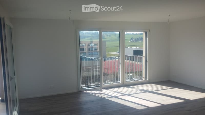 Empty room with wooden flooring, large sliding glass doors leading to a balcony, and natural light streaming in.