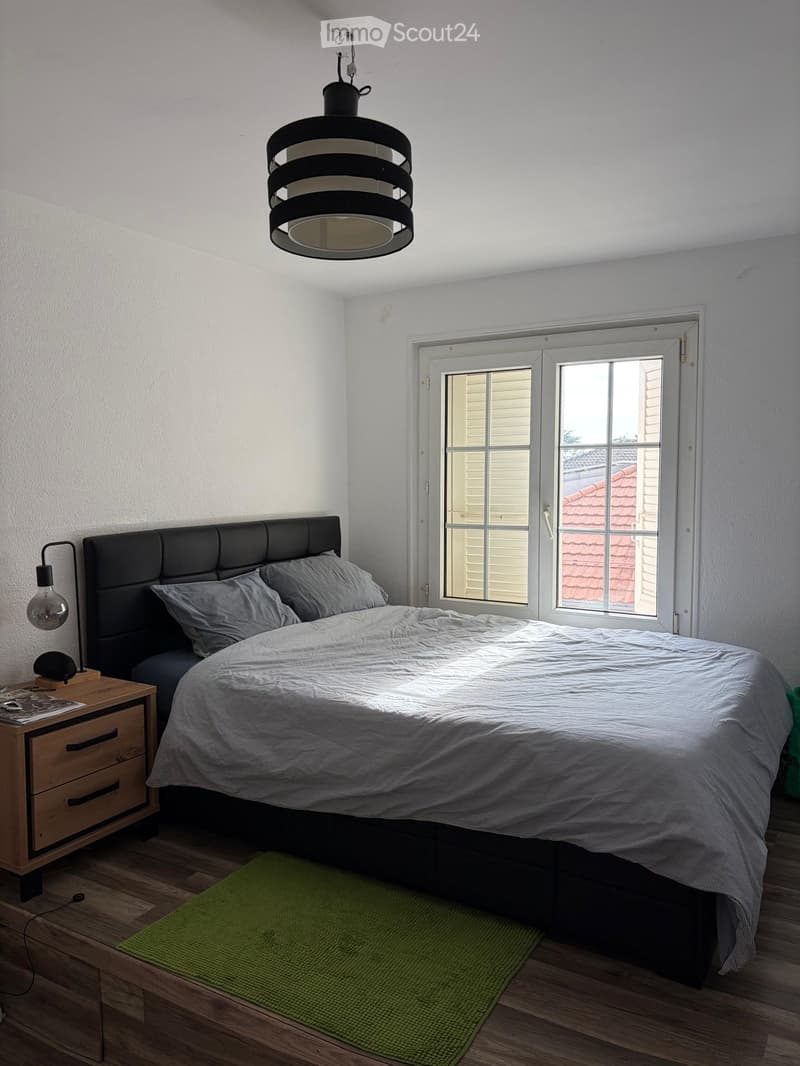 Modern bedroom with a large bed, nightstand, pendant light, and a window with blinds.