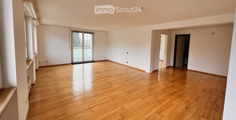 Empty room with wooden flooring, white walls, large sliding glass door leading to a balcony, and a doorway to another room.