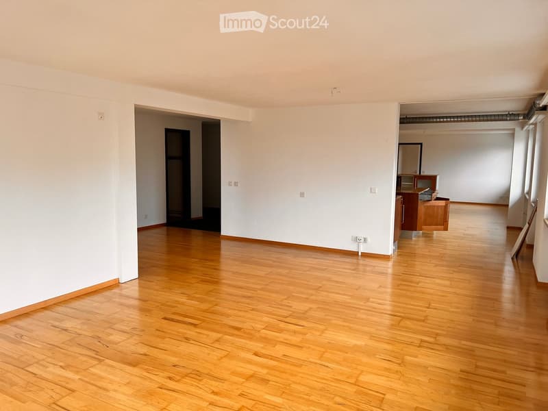 Empty room with wooden flooring and white walls, featuring a doorway leading to another room with a small cabinet and mirror.