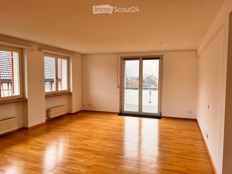 Empty room with wooden flooring, large windows, and a sliding glass door leading to a balcony.