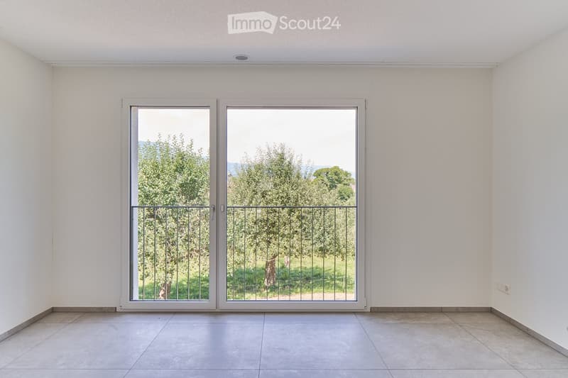 Empty room with white walls, tiled floor, and large sliding glass doors leading to an outdoor area with trees.