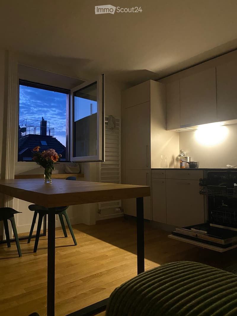 Modern kitchen with wooden floor, large window, built-in cabinets, and a dining table with stools.