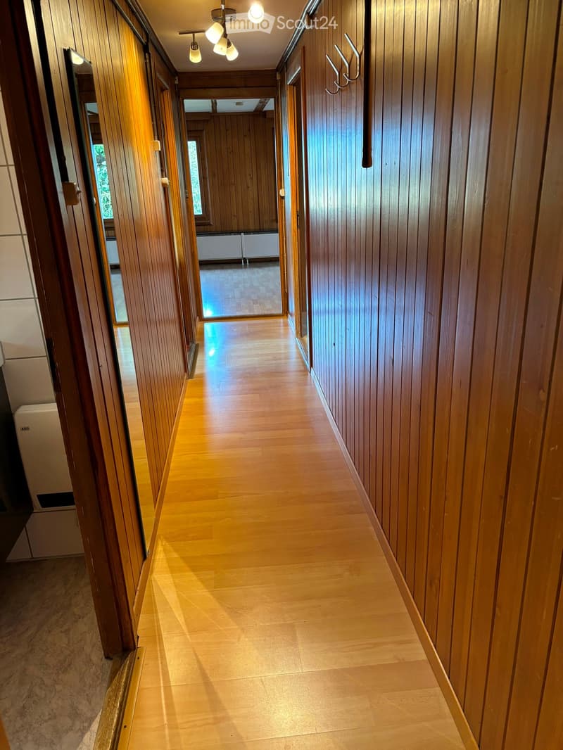 Wooden-paneled hallway with polished wooden floor, recessed lighting, and multiple doors leading to rooms.