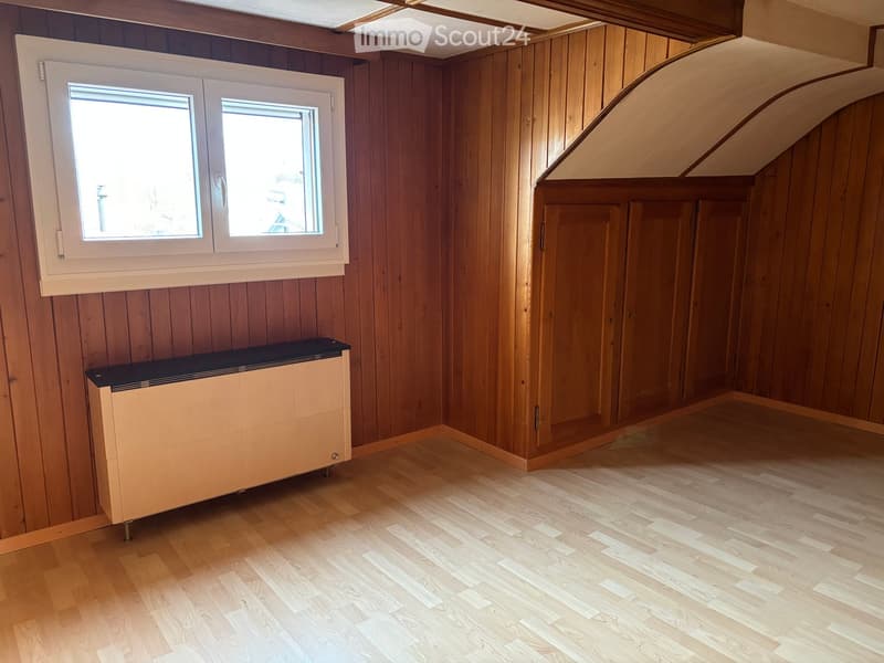 Empty room with wooden walls and flooring, featuring a radiator and a window with white frame.