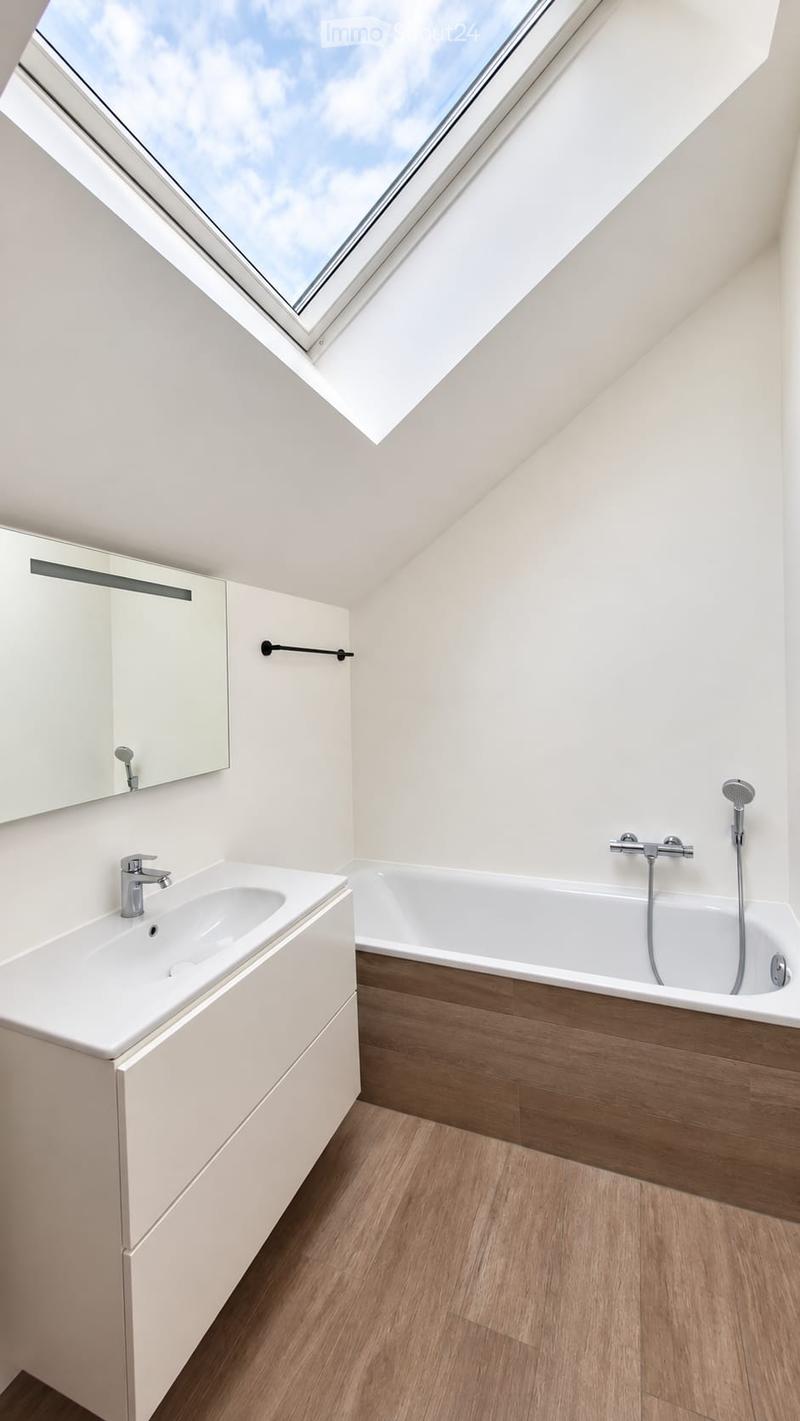 Modern bathroom with a white sink, bathtub, and large skylight window. Features a sleek, minimalist design with wooden flooring and white cabinetry.