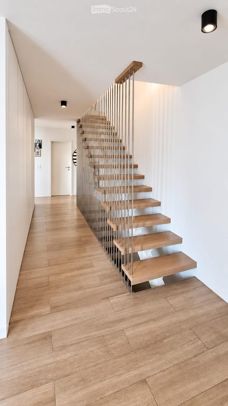 Modern hallway with wooden flooring, a staircase featuring wooden steps and metal railings, white walls, and recessed lighting.