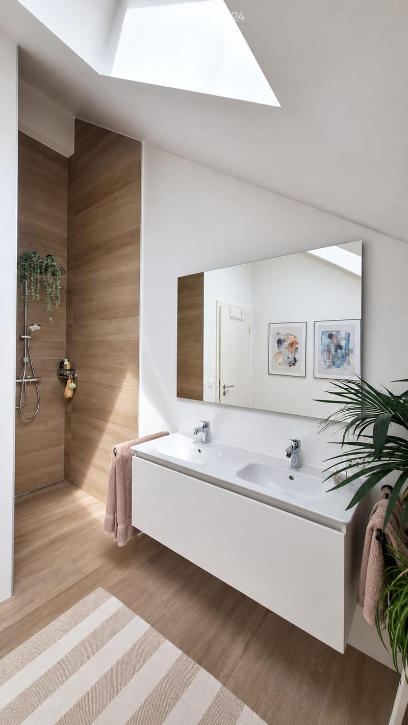 Modern bathroom with a white sink, large mirror, wooden floor, and a small plant in the corner.