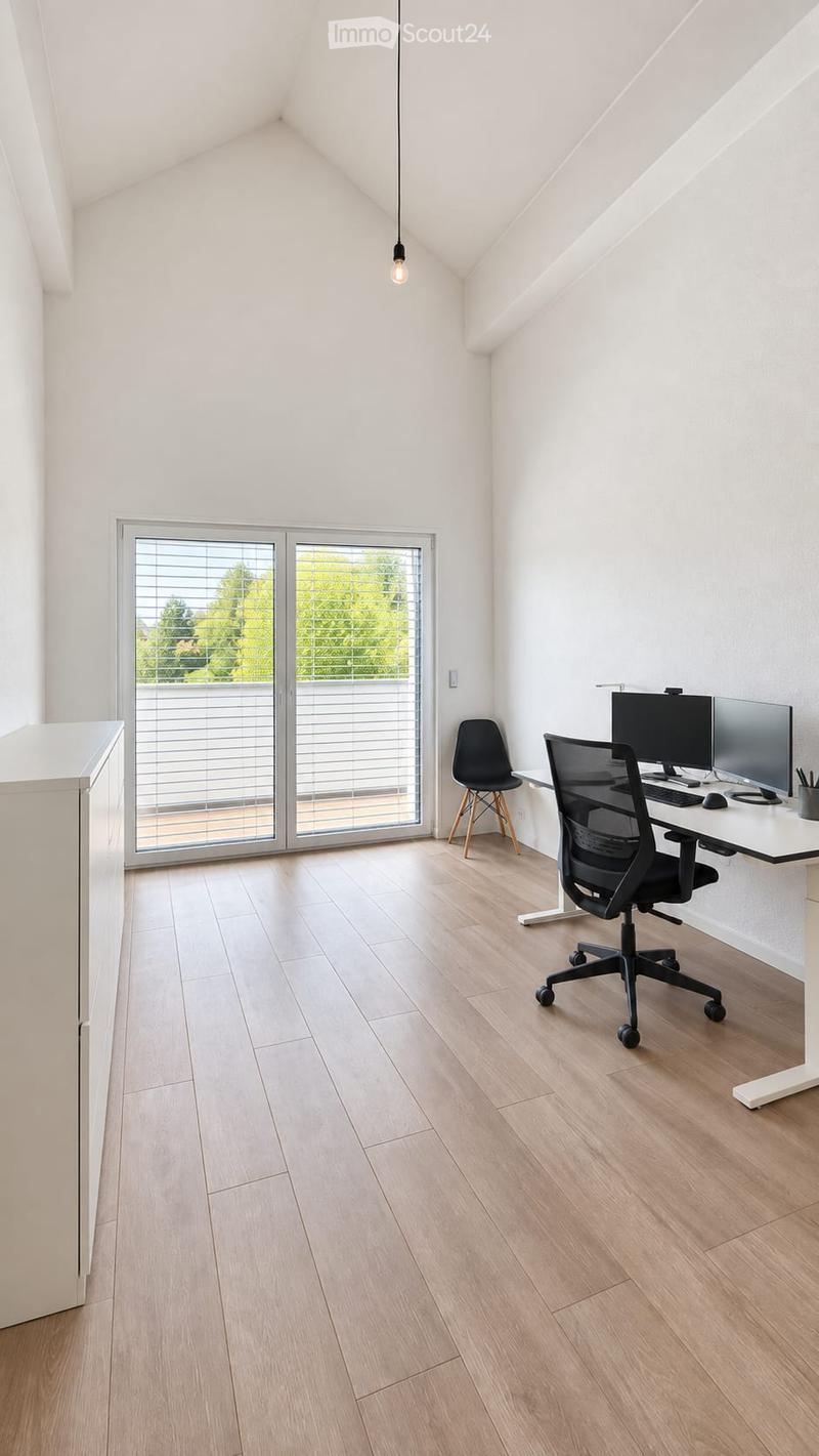 Modern, well-lit room with light wooden flooring, white walls, and a large window with blinds. Contains a desk with a computer setup, two chairs, and a pen holder.