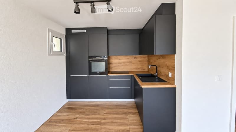 Modern kitchen with dark grey cabinets, wooden countertops, and a built-in oven. Features a sink with a modern faucet and a small window above the sink.