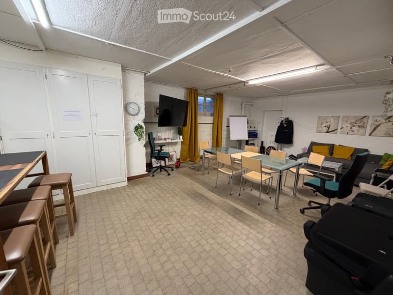 A multi-purpose room with a sofa, chairs, a glass table, and a screen, featuring a tiled floor and exposed ceiling beams.