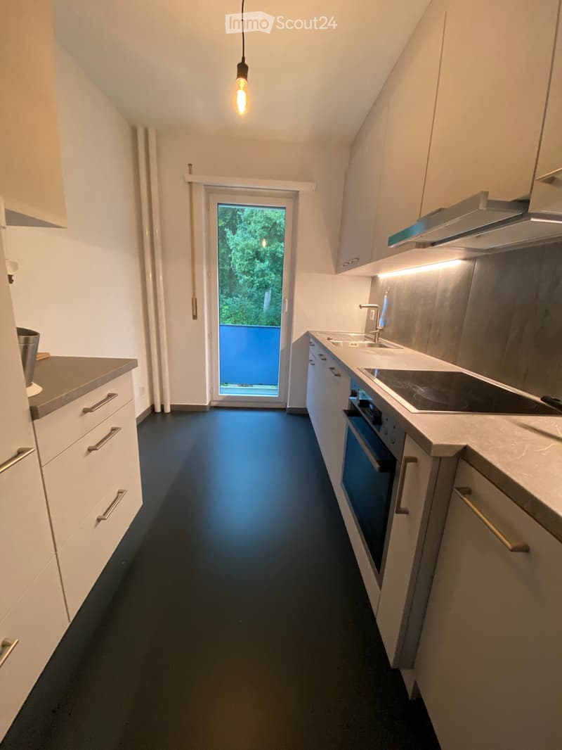 Modern kitchen with white cabinets, dark blue floor, stainless steel appliances, and a view through a glass door to a balcony.