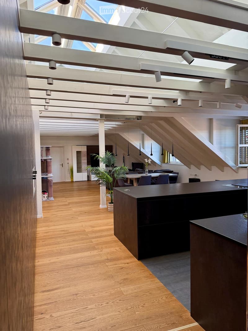 Open-plan office space with wooden flooring, reception desk, chairs, table, sofa, potted plants, and a staircase leading to an upper level.