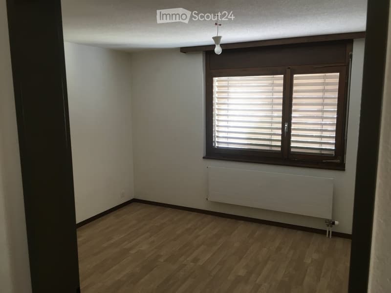 Empty room with wooden flooring, white walls, a window with blinds, and a radiator below the window.