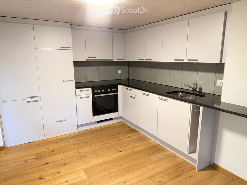Modern kitchen with white cabinets, black countertops, wooden flooring, and stainless steel appliances including an oven and sink.