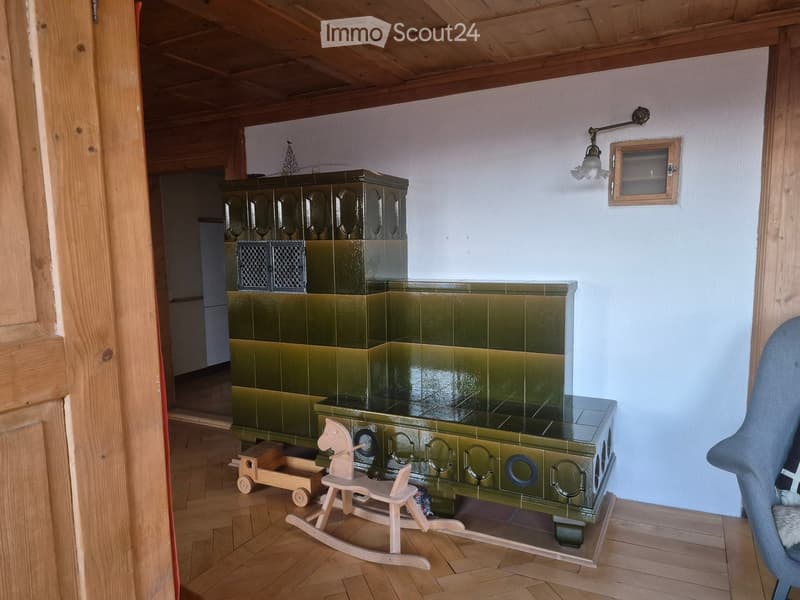 Cozy room with a traditional green tiled fireplace, wooden rocking horse, toy wagon, and a grey armchair near the wall.