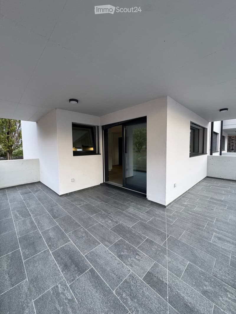 Modern balcony with grey tiled flooring, white walls, large windows, and a sliding glass door leading to an indoor space.