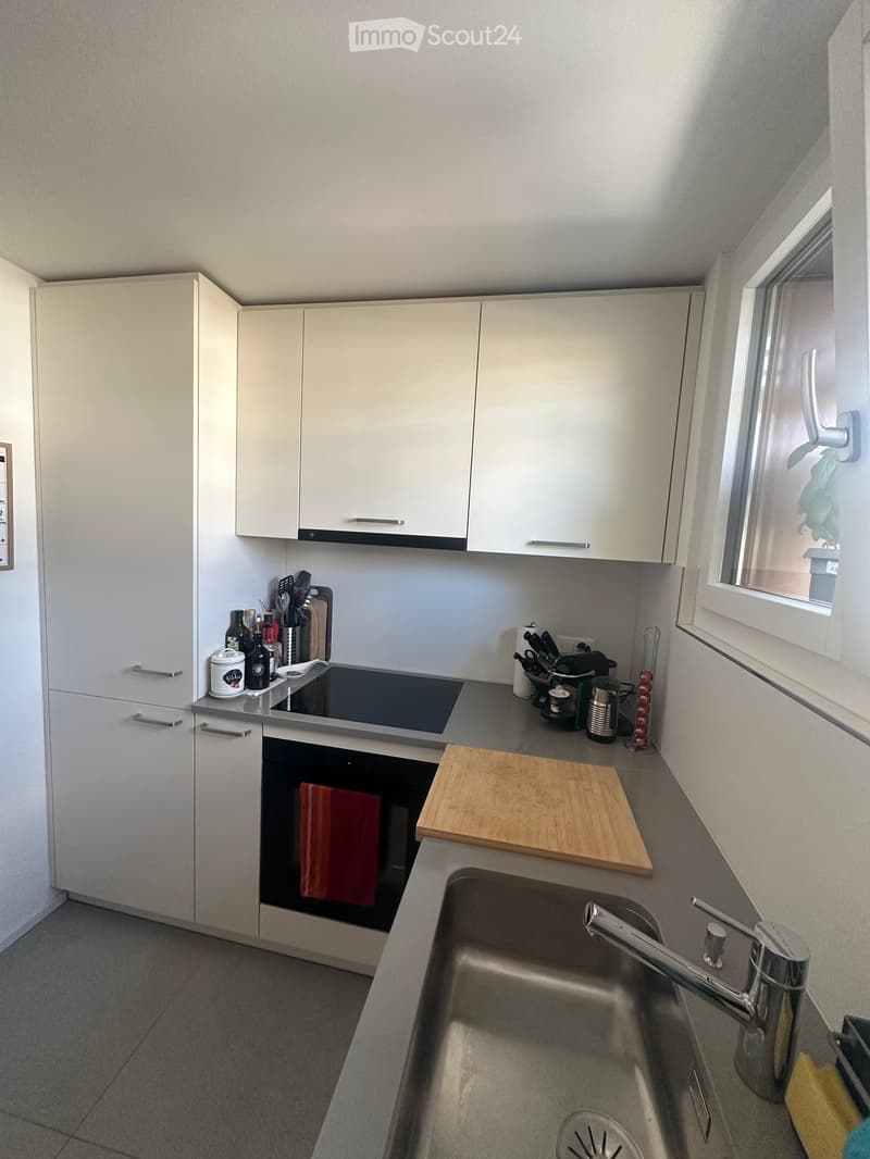 Modern kitchen with white cabinets, stainless steel sink, oven, and various kitchen items on the counter.