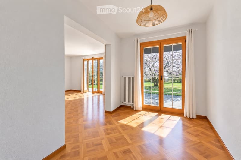Empty room with wooden flooring, white walls, large sliding glass doors, and a hanging woven light fixture.