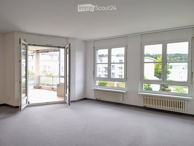 Empty room with large windows, radiators, and an open door leading to a balcony.