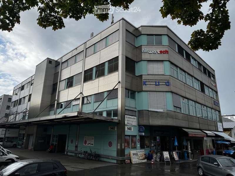 Modern multi-story building with a combination of glass and metal facade, featuring commercial signage and storefronts at the ground level.