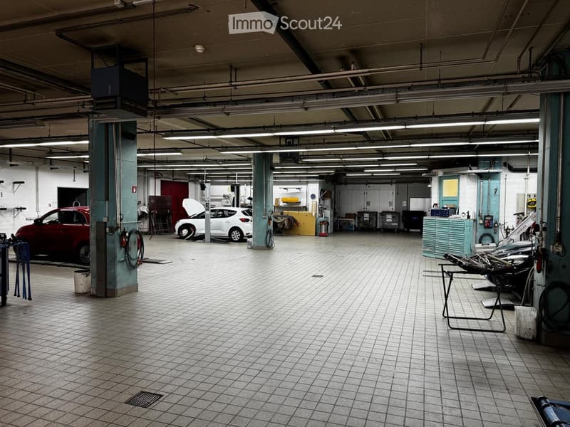Garage with tiled floor, fluorescent lighting, two cars (one with hood open), tool cabinets, and workbenches.