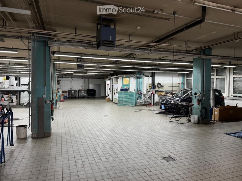 A spacious, well-lit garage with tiled flooring, multiple cars, tool cabinets, workbenches, and storage bins.