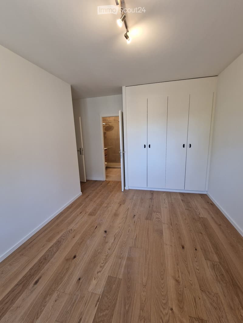 Empty room with light wooden flooring, white walls, built-in white wardrobes, and an open doorway leading to a bathroom.