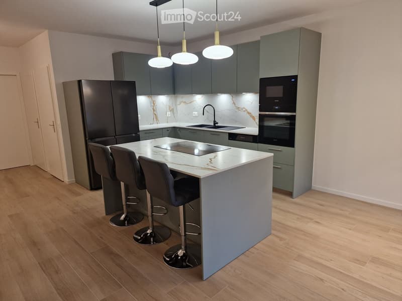 Modern kitchen with grey cabinets, marble countertops, stainless steel appliances, and pendant lights above the island.